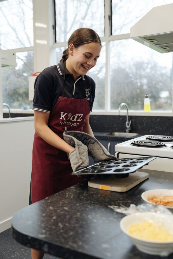Smiling young woman in an apron baking muffins in a modern kitchen.